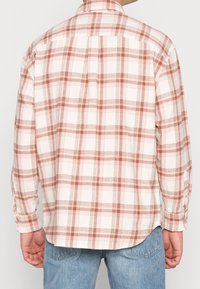 Koszula w kratę w jasnym kremowym kolorze z ciepłymi różowymi i brązowymi kratkami, z długimi rękawami, mankietami na guziki oraz klasycznym kołnierzykiem, z zaokrąglonym dołem.