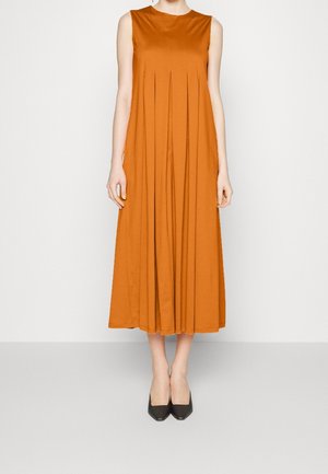 Robe midi sans manches orange brûlé avec plis devant, portée avec des talons noirs à bouts pointus, mannequin debout sur fond blanc uni.