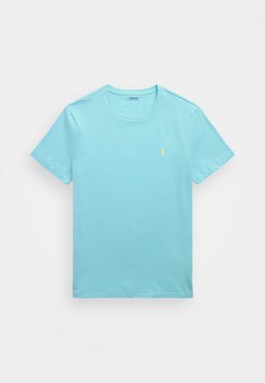 Camiseta de algodón azul cielo con mangas cortas, cuello redondo y un pequeño logo bordado amarillo en el lado izquierdo del pecho. Textura suave, diseño casual.