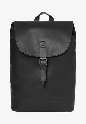 Musta nahkainen reppu, jossa on läppä, joka suljetaan solkivyöllä, ja yläkahva. Edessä on hillitty Eastpakin logo.