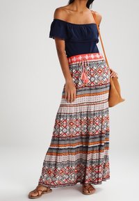 Marinblus utan axlar med volang, i kombination med en mönstrad maxikjol i orange, röd, svart och vit, med dragsko i midjan.