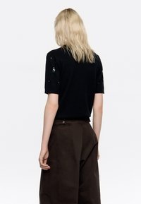 Suéter negro de mangas cortas, adornado con lentejuelas en los hombros, combinado con pantalones de pierna ancha de talle alto en color marrón.