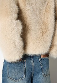 Beige nep-bont kort jasje met een fluffy textuur. Gecombineerd met high-waisted, vervaagde blauwe denim jeans met achterzakken.