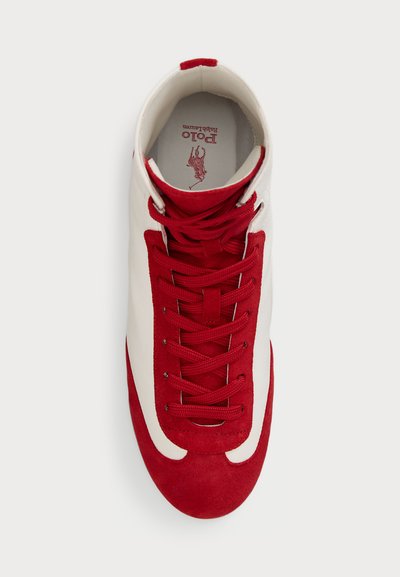 Weißer und roter Sportschuh mit einem glatten Lederoberteil, strukturierten roten Wildlederakzenten und roten Schnürsenkeln, mit einem Logo auf der Innensohle.