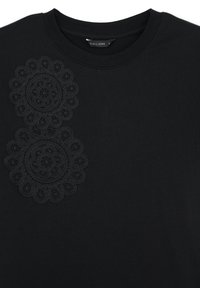 T-shirt in cotone nero con scollo rotondo, caratterizzata da due grandi motivi floreali circolari ricamati in nero nella parte superiore sinistra del petto.