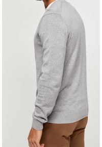 Pull en maille gris à manches longues, col rond, poignets et ourlet côtelés, texture lisse, silhouette ajustée, associé à un pantalon marron.