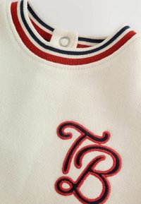 Witte sweatshirt met een gestructureerde stof en ribgebreide halslijn in rood, marineblauw en wit. Voorzien van een opvallend geborduurd 'TB'-logo in het rood.