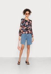 Blusa floral de manga longa em preto, com flores rosas e azuis. Combinada com calções de ganga claros e bolsa rosa, completada com sandálias pretas.