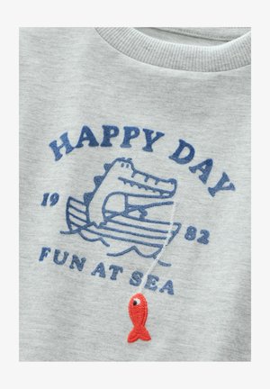 Grå sweatshirt med blått broderat mönster av en krokodil på en båt med vågor, röd fisk som accent och texten "HAPPY DAY FUN AT SEA."