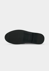 Semelle de chaussure habillée noire avec un talon léger et une texture lisse, vue de dessous sur fond gris clair.