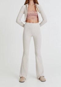 Veste zippée en maille côtelée gris clair à manches longues, associée à un top court rose à motifs et un pantalon évasé assorti avec un ourlet à volants.