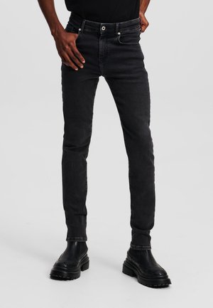 Schwarze Slim-Fit-Jeans aus Denim mit subtilen Ausbleichungen, Vordertaschen und Reißverschluss. Kombiniert mit schwarzen klobigen Stiefeln für einen modernen Look.