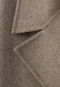 Bruine wollen stof met een zacht, getextureerd oppervlak en overlappende driehoekige rever, met subtiele kleurvlekjes.