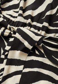 Tissu noir et blanc avec motif imprimé zèbre, froncé au centre avec un nœud ou un détail torsadé.