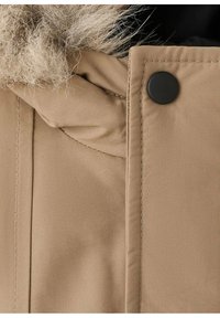 Gabardina de invierno beige con ribete de piel en la capucha, que cuenta con cierre a presión negro y detalles de costura visibles.