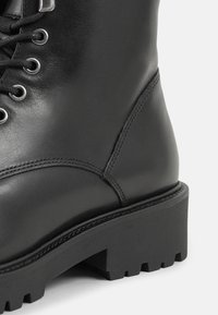 Stivale alla caviglia in pelle nera con punta rotonda, design con lacci, occhielli metallici e suola in gomma robusta con modelli di battistrada profondi.