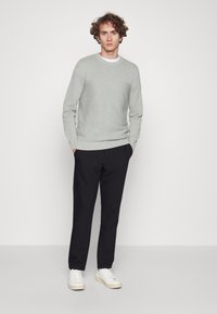 Grijs textuurtrui met lange mouwen en een ronde hals; gecombineerd met zwarte broeken en witte sneakers. Eenvoudig ontwerp, geen zichtbare patronen of accenten.