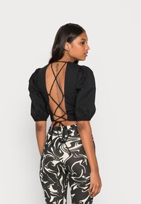 Top preto curto com mangas bufantes e costas abertas com rendas, combinado com calças de cintura alta com padrão marmoreado em preto e creme.