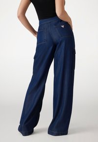 Pantaloni cargo a gamba larga in denim scuro, con vita alta, tasche frontali e un piccolo dettaglio con logo sulla tasca posteriore.