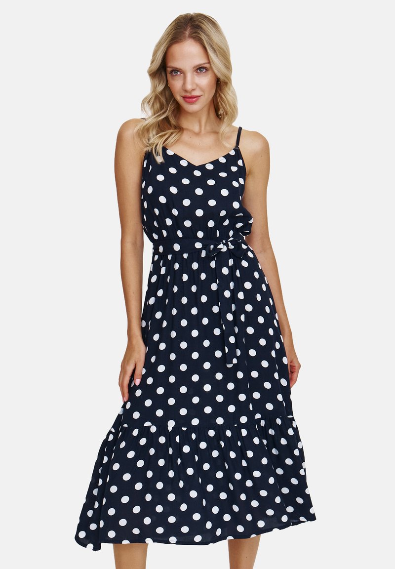 Granatowa sukienka bez rękawów w białe kropki, z dekoltem w kształcie litery V, dopasowana w talii z wiązaniem, oraz z falbanowym dołem w warstwach.