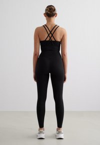 Melnā sporta krūšturis ar krustveida siksnām, apvienots ar augsto jostasvietu melnajām legingām. Gluda faktūra, pieguļošs dizains, minimāls detalizējums un potītes garums.