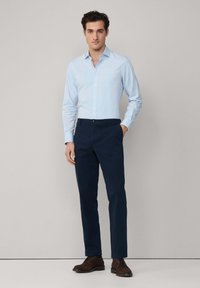 Lichtblauw overhemden met lange mouwen, gecombineerd met donkerblauwe broeken en bruin leren schoenen. Gladde stof, slim fit, strakke lijnen.