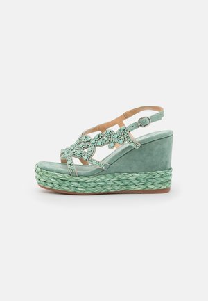 Myntegrøn kilehæl sandal med flettet platformsål, perlebesatte dekorative stropper og justerbar ankelspænde, vist fra siden.