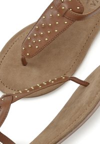 Ruske nahkasta valmistetut sandaalit kultaisilla niiteillä päällisessä, joita korostaa pehmeä tan-suede sisäpohja ja kaareva tan-ulkopohja mukavuutta varten.