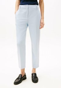 Jasnoniebieskie spodnie o dopasowanym kroju, z bocznymi kieszeniami, zestawione z czarnymi loafersami. Gładki materiał i czyste linie.