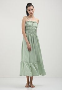 Light green, maxi dress made of soft fabric. Features smocked bodice, thin straps, and a tiered skirt. Simple and flowy design.