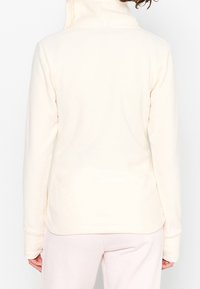 Pullover in pile color crema con colletto alto, maniche lunghe e texture liscia. Presenta un orlo arrotondato e senza chiusure visibili.