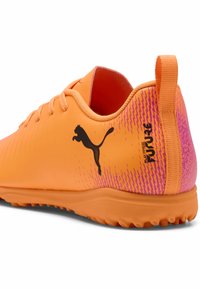 Scarpa sportiva arancione con tomaia texturizzata e tallone sfumato in rosa. Presenta logo e etichetta neri. Suola in gomma per una migliore aderenza. Design leggero.