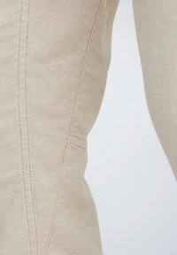 Beige stof met zichtbare stiksels, met een gladde textuur en gevormde vorm, die een getailleerd ontwerp benadrukt.