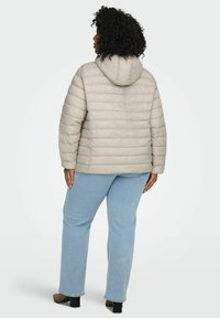 Bēšs pūkains mētelis ar kapuci, horizontāla šūta dizaina, ar garām piedurknēm, kombinēts ar gaiši zilām džinsām un apaviem ar bloka papēdi.