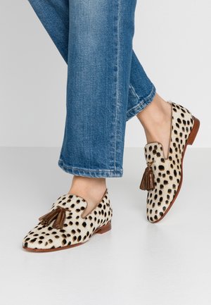 Lofers z futrzanym wykończeniem w panterkę, z brązowymi frędzlami i płaską podeszwą, zestawione z podwiniętymi niebieskimi dżinsami.