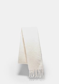 Écharpe blanche en matériau doux, présentant une surface texturée, des bords frangés et un petit emblème décoratif près d'une extrémité.