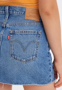 Leren denim mini-jurk in lichtblauw met een franjerand. Bevat een beige leren label en een kenmerkend stikselpatroon op de achterzak.