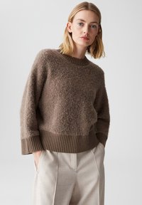 Brauner, strukturierten Pullover mit einem gerippten Rundhalsausschnitt und Bündchen, kombiniert mit hellbeigen, gefalteten Hosen. Weiches, kuscheliges Material.