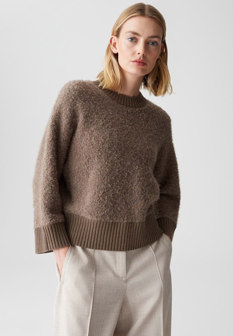 Brauner, strukturierten Pullover mit einem gerippten Rundhalsausschnitt und Bündchen, kombiniert mit hellbeigen, gefalteten Hosen. Weiches, kuscheliges Material.