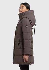 Padded brown parka with a high collar, zippered pockets, and a logo on the sleeve. Features a hood with drawstrings and a sleek design.