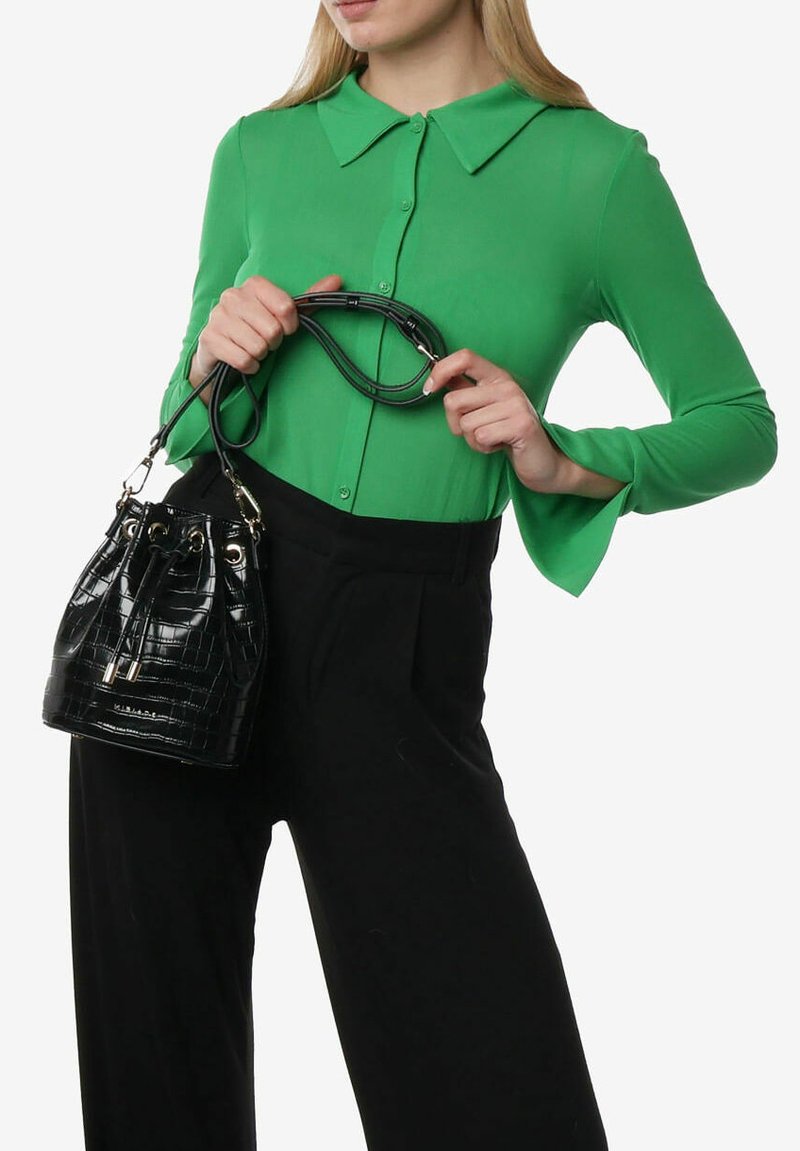 Borsa a secchiello nera in pelle stampata coccodrillo con doppi manici, hardware metallico e chiusura a coulisse, abbinata a una camicetta verde con colletto e pantaloni neri.