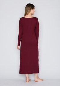 Camisón de manga larga color burdeos hecho de tela suave y elástica con un ajuste relajado, que presenta un escote en forma de U en la espalda y un dobladillo hasta el tobillo.