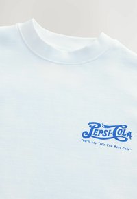 Sweatshirt en coton blanc avec un col rond et un logo Pepsi-Cola bleu vif avec slogan, positionné sur la zone gauche de la poitrine.