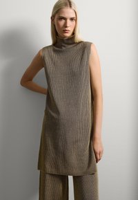Túnica sin mangas y de cuello alto en tejido texturizado de color marrón dorado con líneas verticales, combinada con pantalones de pierna ancha a juego. Diseño simple pero elegante.