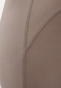 Nærbillede af beige stof med buede syninger, der danner en glat, tætsiddende overflade, der fremhæver syningsdetaljer og tekstur.