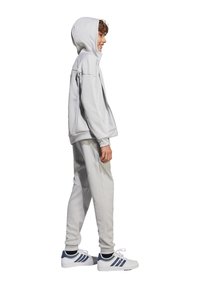 Hellgraues Sportoutfit mit einer Kapuzenzip-Jacke und passenden tapered Pants. Der Stoff hat eine glatte Textur, sitzt locker und hat gerippte Bündchen.