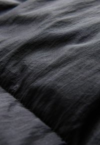 Tela negra con una textura suave y pliegues visibles, que presenta una superficie ligeramente brillante y una costura cosida que atraviesa el centro.