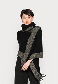 Châle noir avec une rayure texturée or et noire, doté de bords à franges. Matière douce avec un design drapé et un col haut.