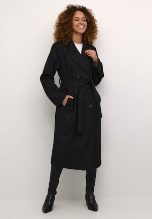 Palton negru cu două rânduri de nasturi, cu talie accentuată printr-un brâu, buzunare laterale și mâneci lungi. Textură netedă, design până la genunchi.