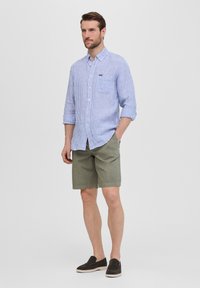 Camisa de botones a rayas azul claro y blanca con mangas largas, combinada con pantalones cortos verdes oliva y zapatos oscuros tipo slip-on.